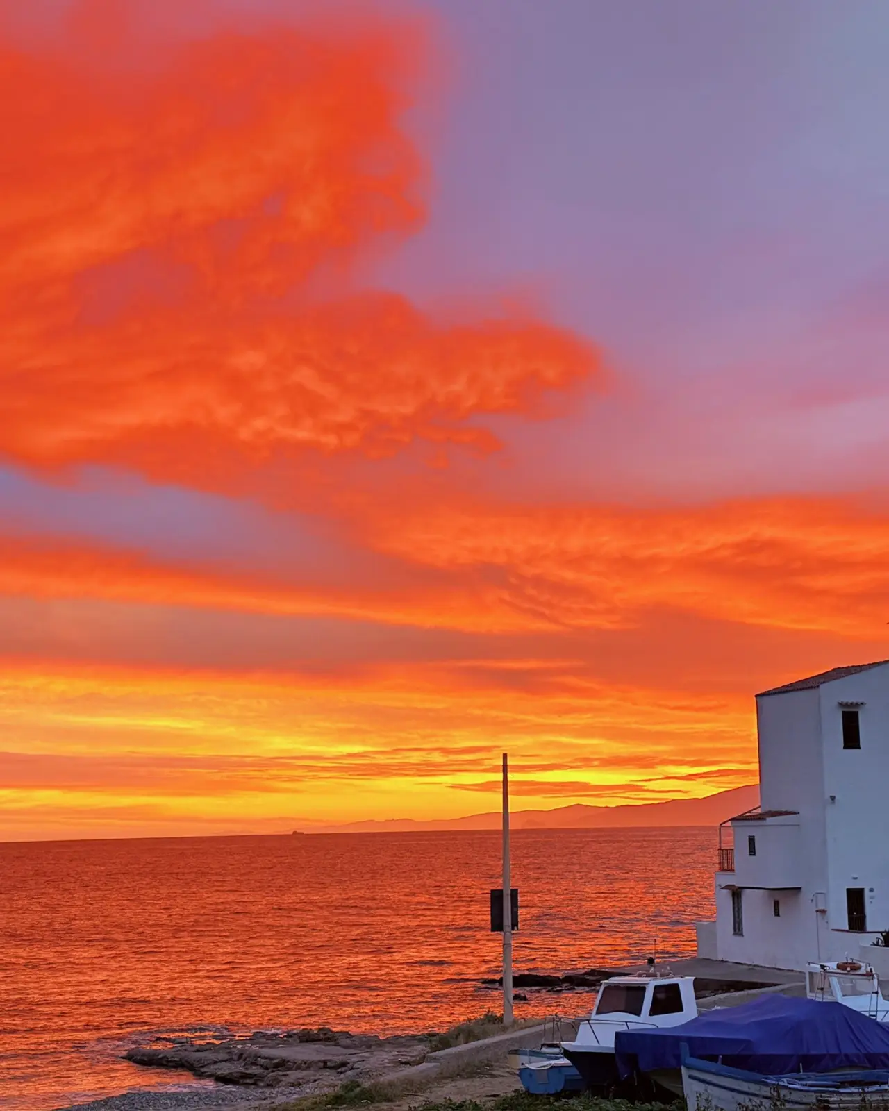Sonnenuntergang über dem Meer, am Ufer ein weißes Haus und Fischerboote