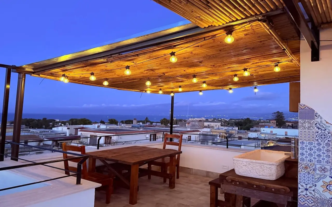 Pergola mit Lichterketten und Holztisch, im Hintergrund das Meer