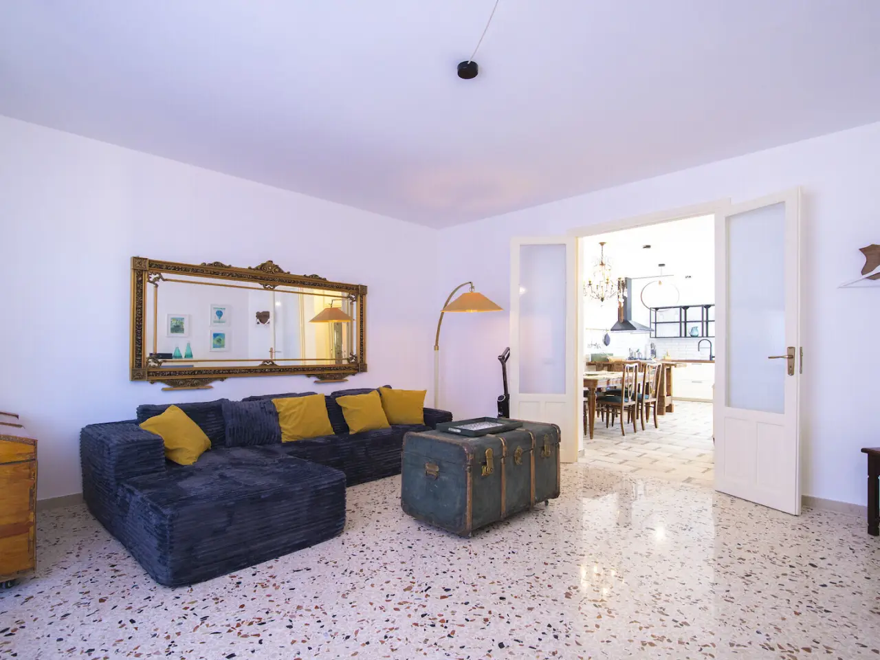 Wohnzimmer mit dunkelblauem Sofa, gelben Kissen und Terrazzoboden
