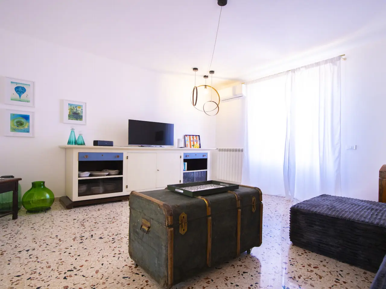 Wohnbereich mit Truhentisch, Fernseher und Keramikbildern