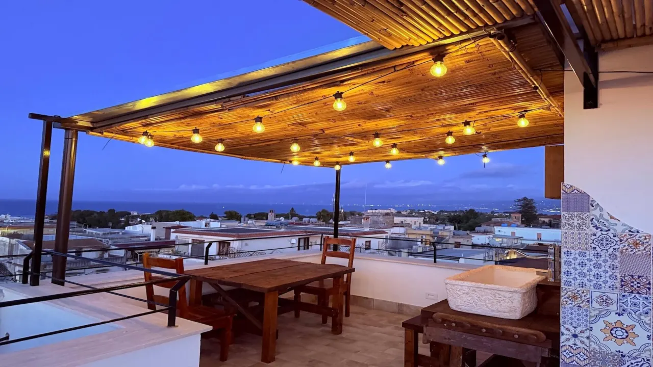 Pergola mit Lichterketten und Holztisch, im Hintergrund das Meer